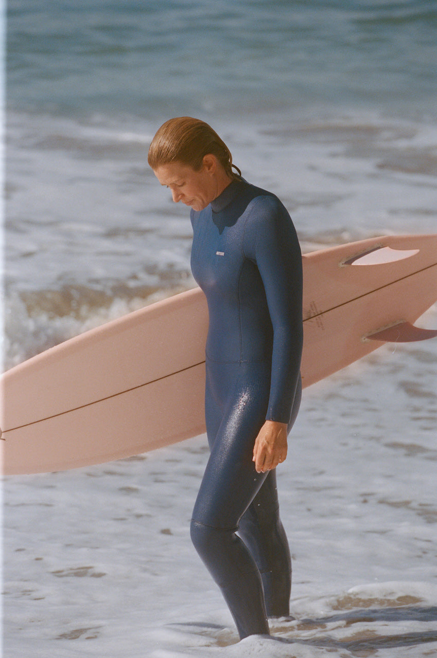 Person in a wetsuit holding a surfboard on a beach