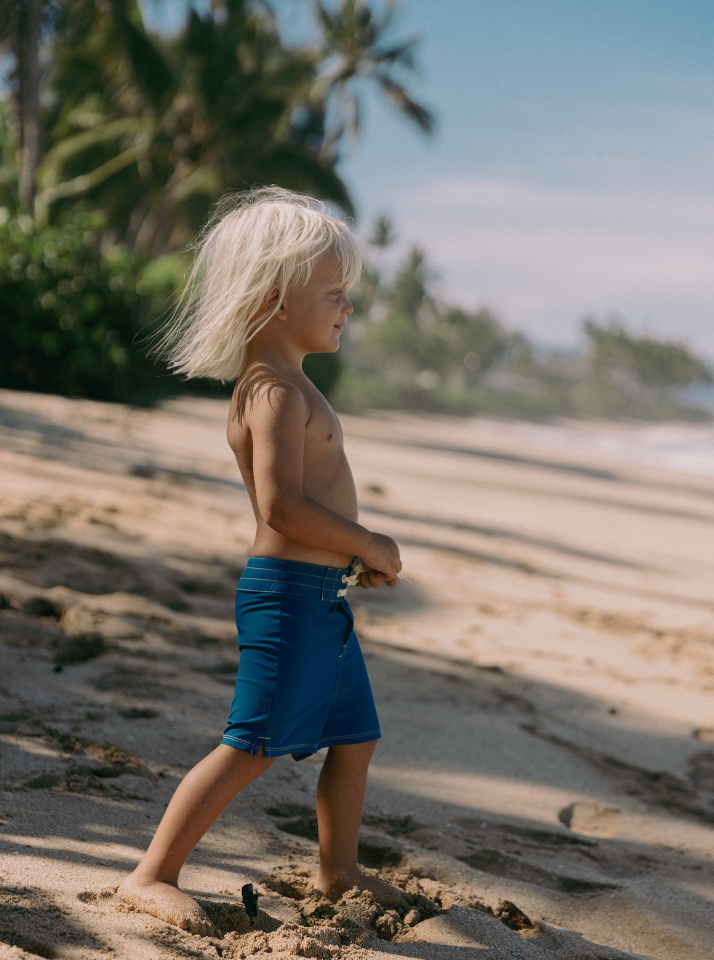 Child walking on a sandy beach with palm trees in the background