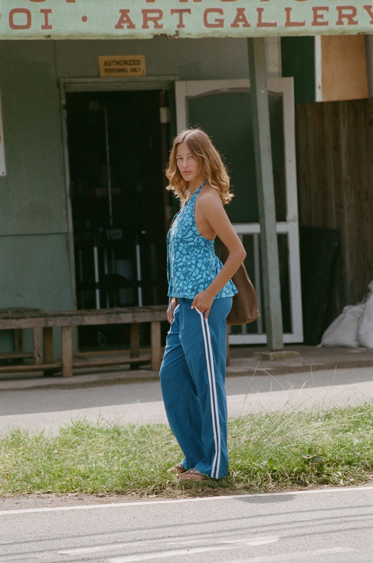 Woman in a blue sleeveless top and pants standing on a street in front of an art gallery.