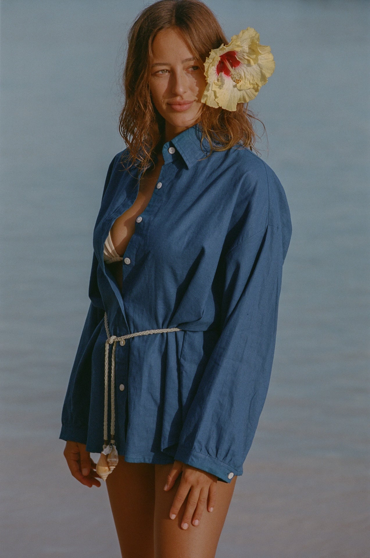 Woman wearing a blue shirt with a belt, standing against a blurred natural background