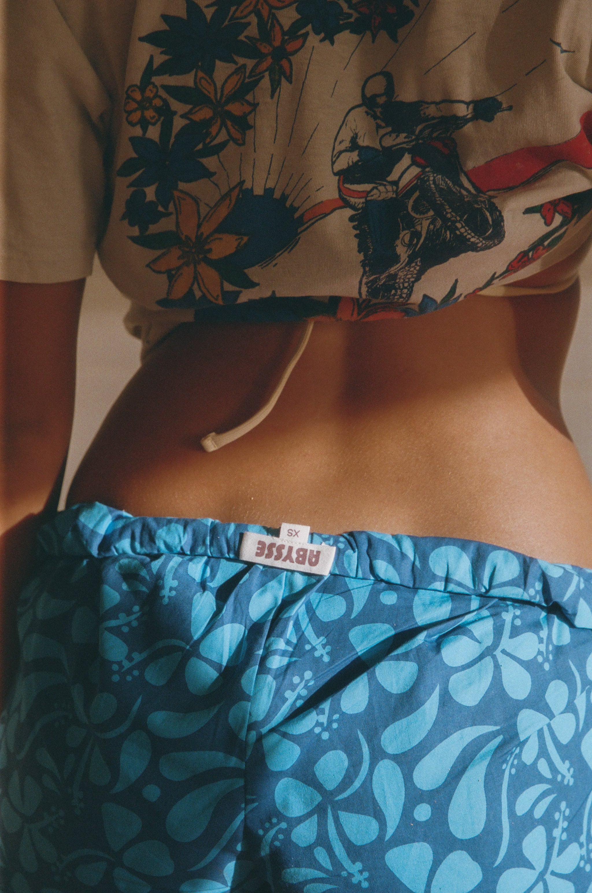 Person wearing a beige shirt with a graphic design and blue patterned shorts.