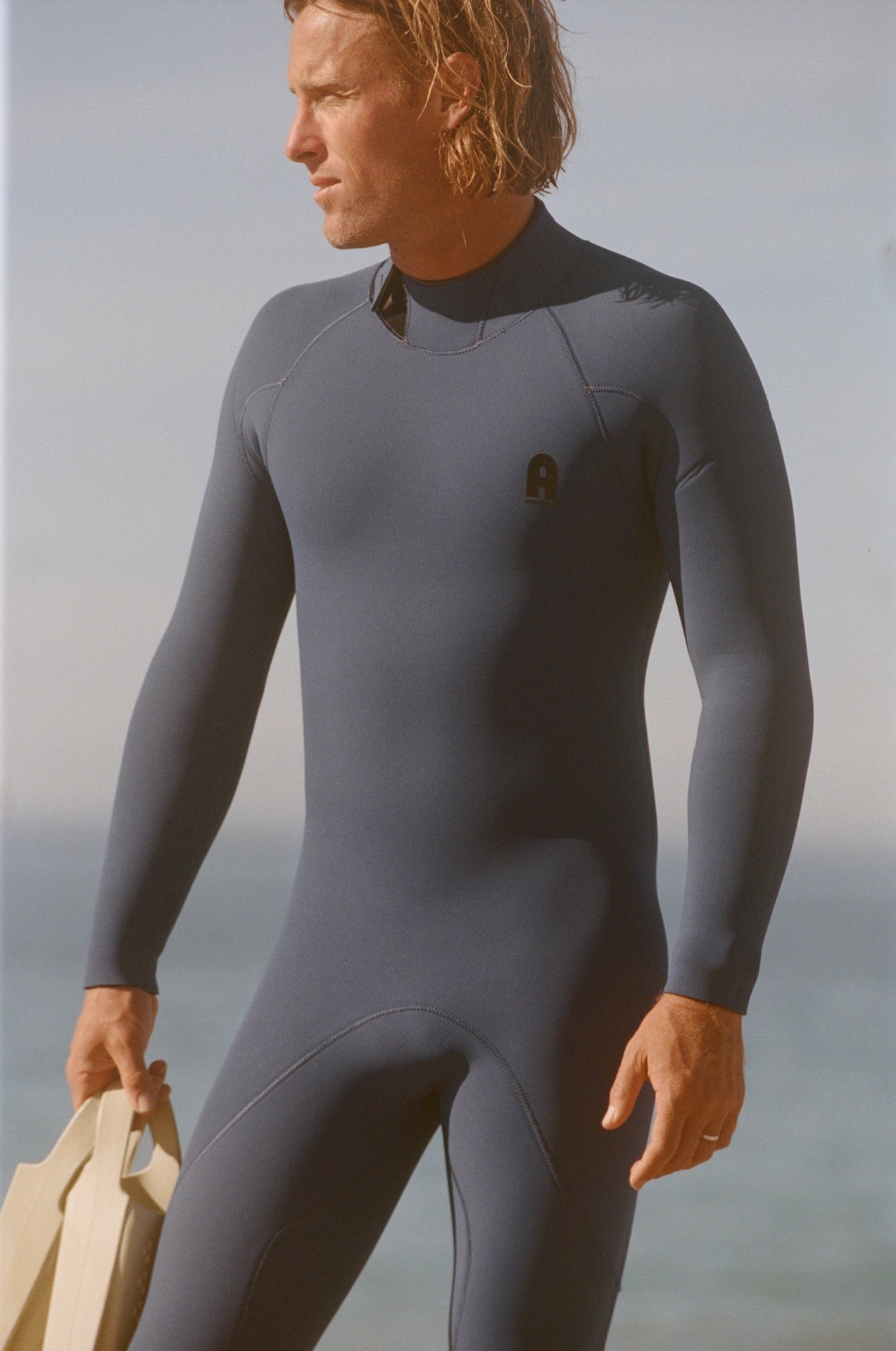 Man wearing a gray wetsuit standing on a beach with ocean in the background