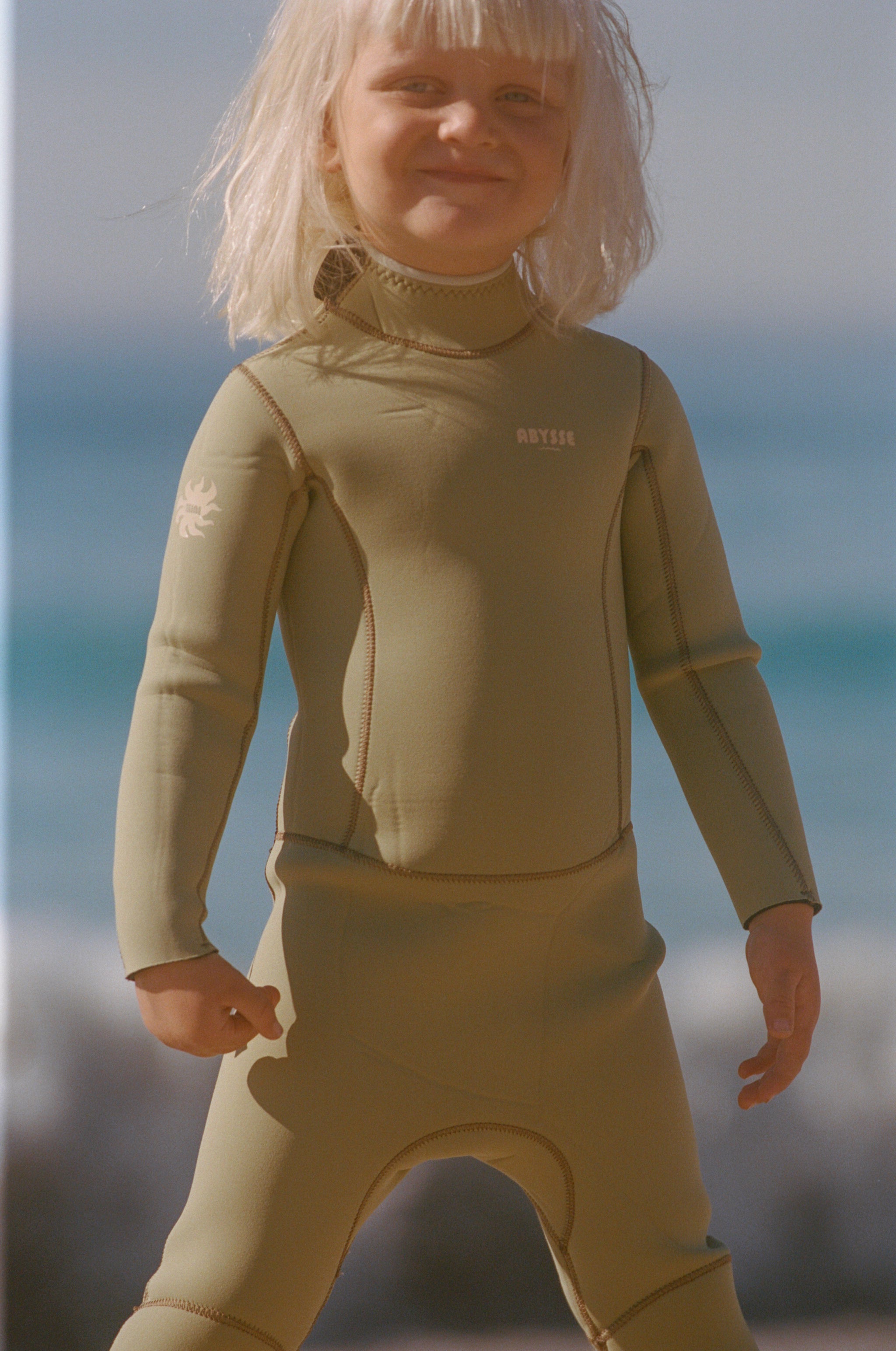 Child wearing a green wetsuit with a blurred beach background