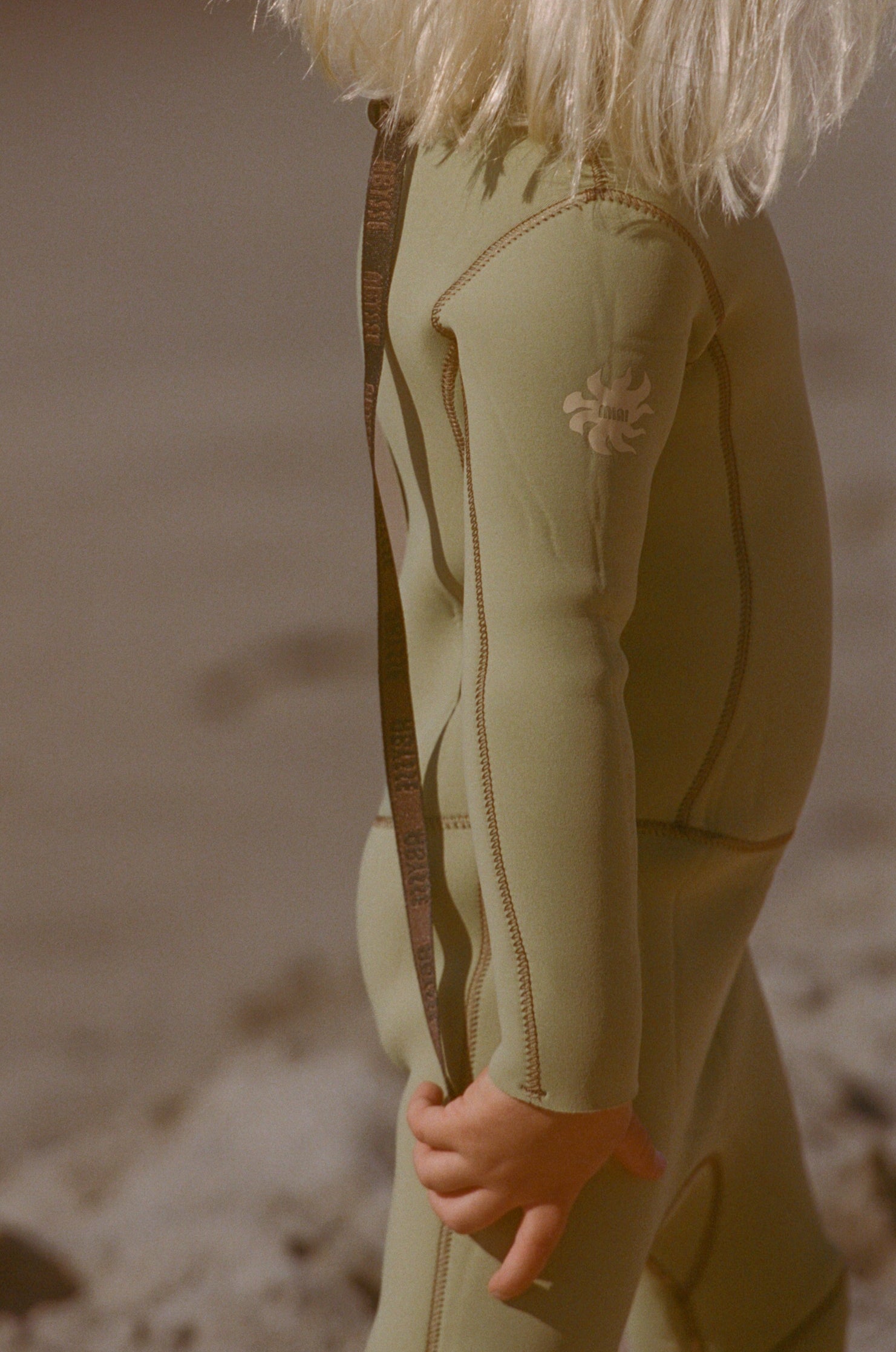 child wearing a green wetsuit on a beach
