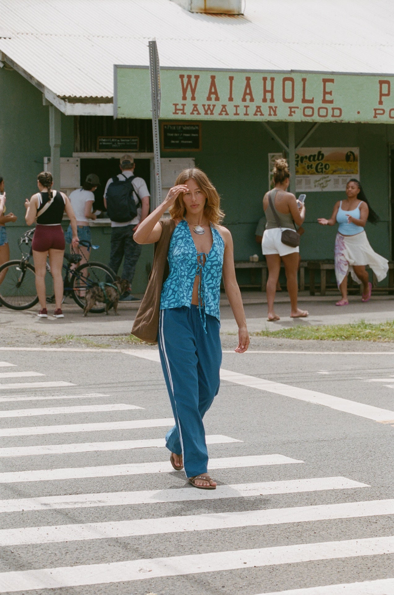 Woman in a blue dress walking on a crosswalk in front of a Waiahole store.