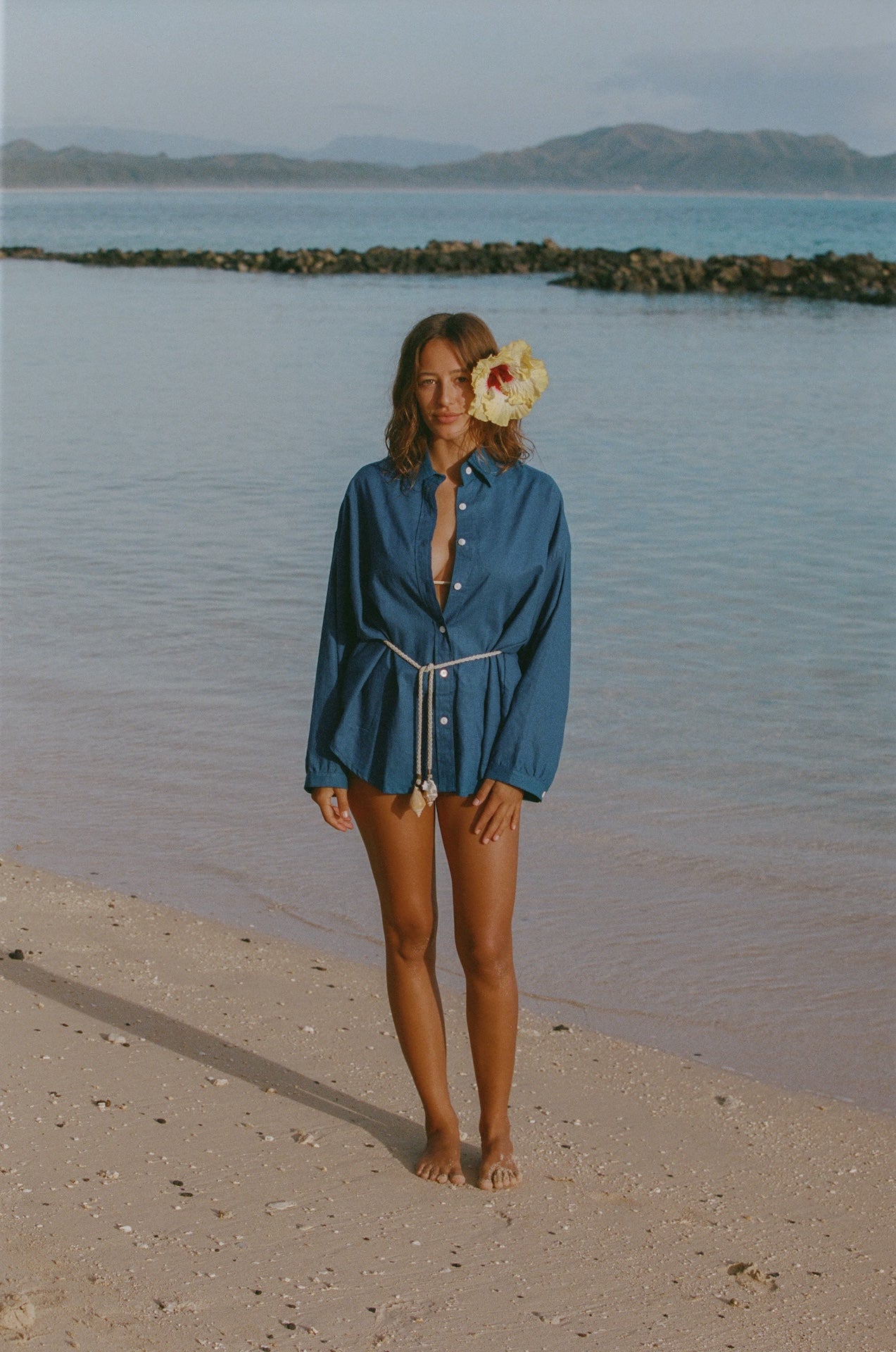 Woman in a blue dress standing on a beach with a flower in her hair