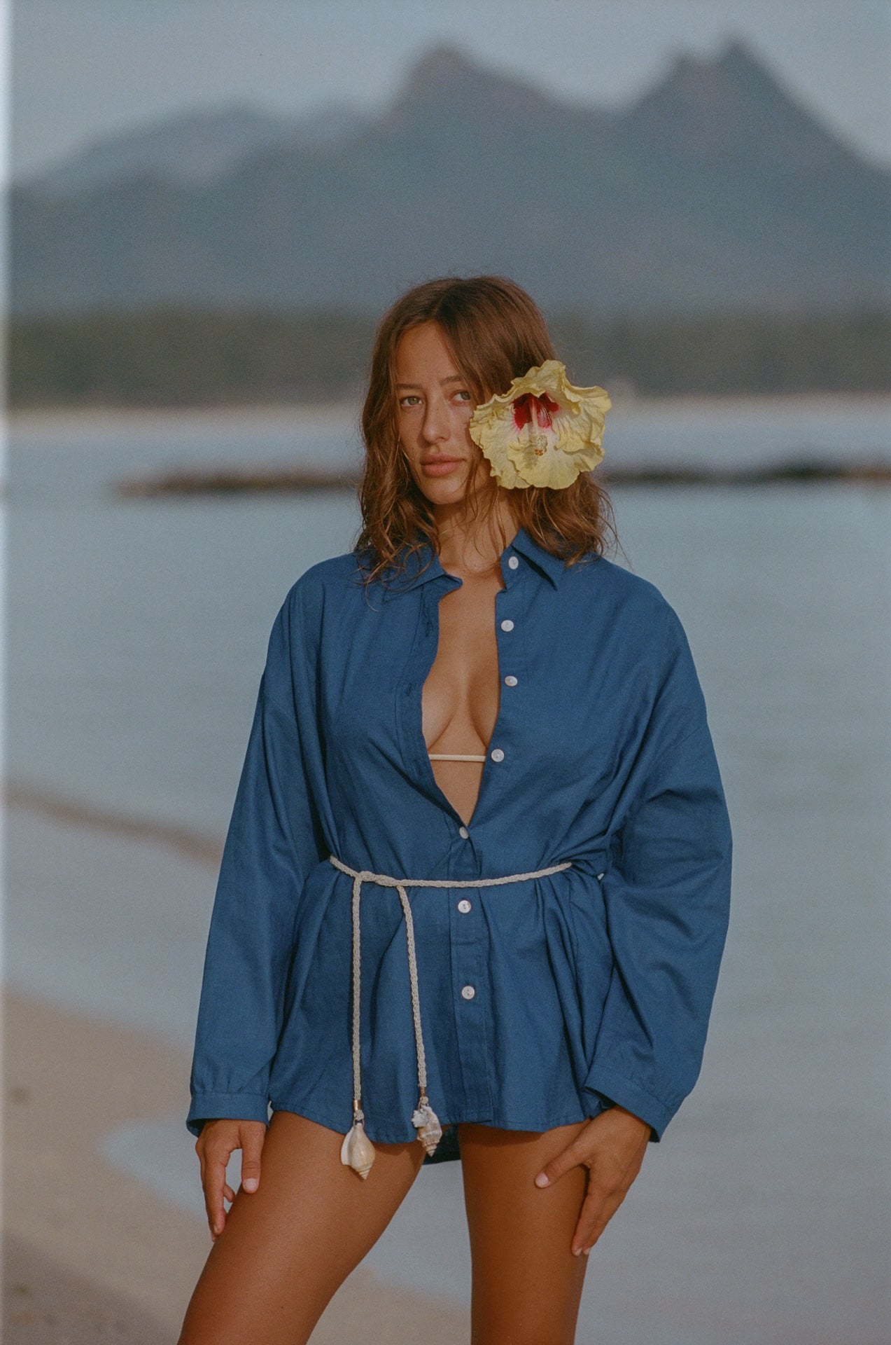 Woman in a blue cover-up standing on a beach with mountains in the background