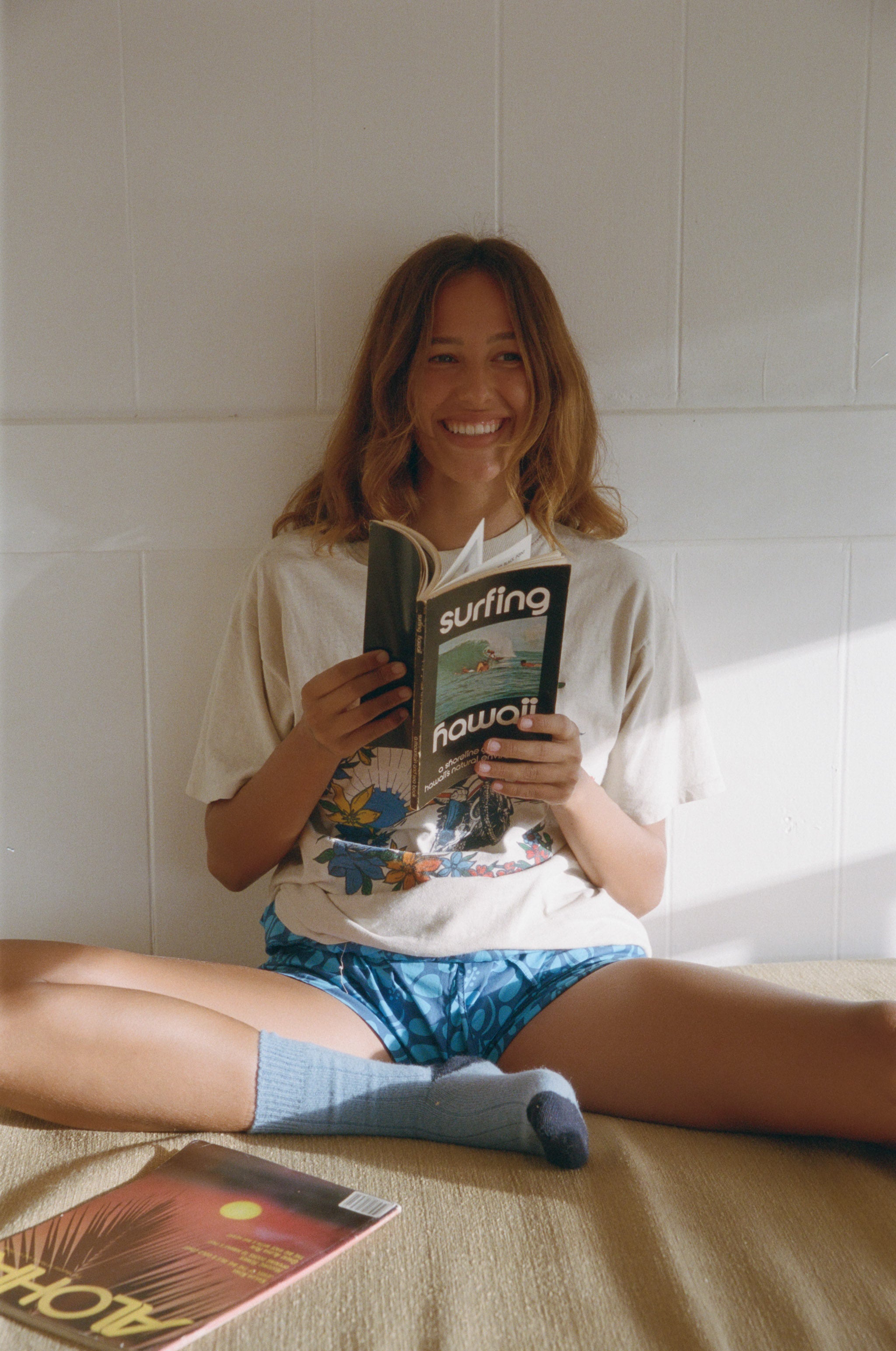 Woman sitting on a bed holding a book with a white wall in the background