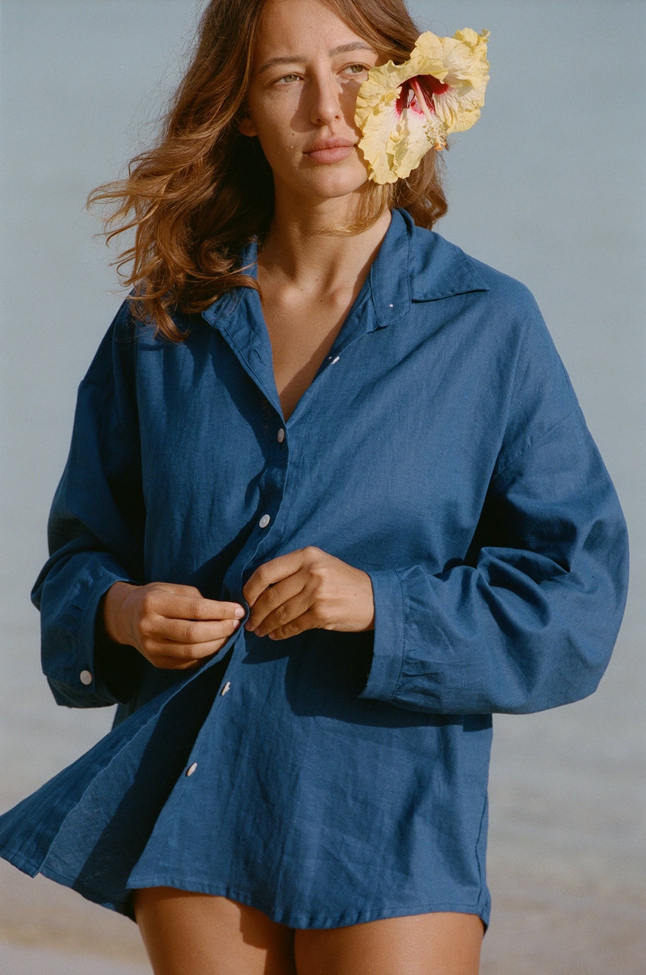 Woman wearing a blue shirt with a yellow flower in her hair against a gray background