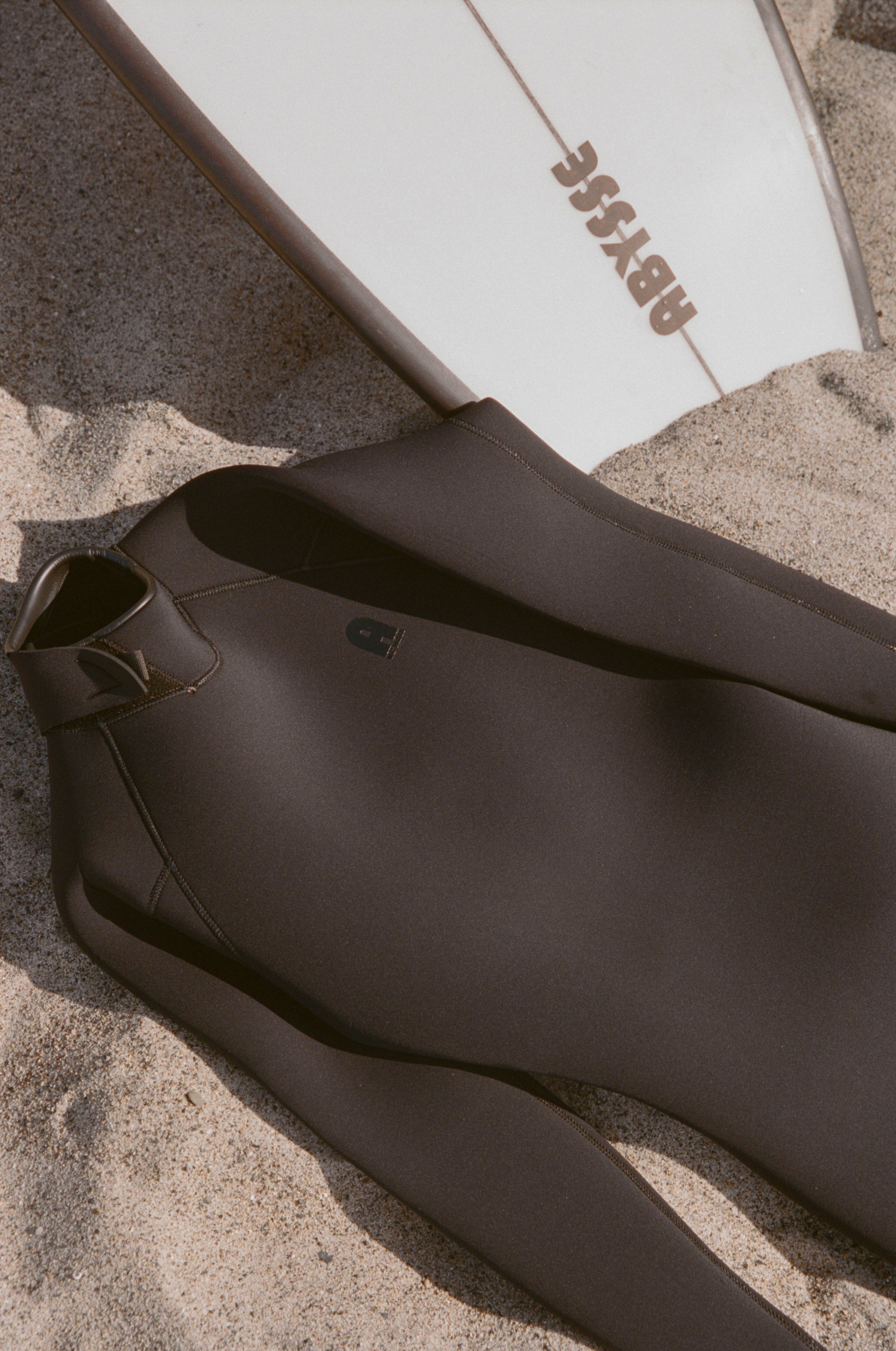 Brown wetsuit on sand with a white board featuring 'BOOG' branding.