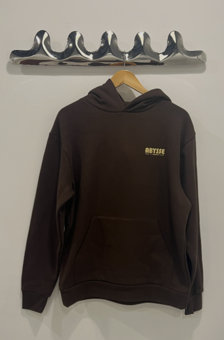 Brown hoodie with a logo on a hanger against a white wall